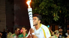 Ygor Marcel da Cruz Santos segura com as duas mãos e beija a tocha olímpica, vestido com o uniforme branco e amarelo utilizado pelos condutores nas Olimpíadasganhar dinheiro slot2016. Ao fundo, há outras pessoas e a folhagemganhar dinheiro slotuma árvore