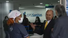 O interior de um prédio de uma EPS mostra funcionários, pacientes e um letreiro com a inscrição “EPS Sanitas”