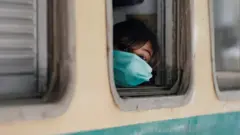A girl wearing a protective mask looks out from a train window in Karachi, Pakistan