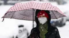 A woman wears a medical mask during a snowfall in a street in February, 2020