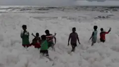 Crianças brincam em espuma em praia na Índia