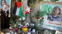 A Palestinian woman takes pictures at the scene where Al Jazeera reporter Shireen Abu Akleh was shot dead during an Israeli raid