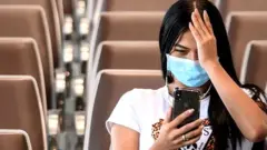 మాస్క్ ధరించి ఐఫోన్ చూస్తున్న యువతి