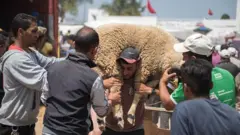 رجل يحمل خروفا على كتفيه استعدادا لعيد الاضحى