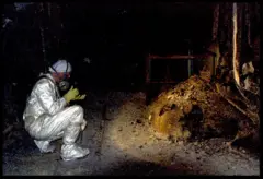 Foto de un investigador agachado tomando una foto de la "pata de elefante", una formación de corio bajo el reactor 4 de Chernóbil.