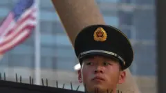 A paramilitary policeman looks on past the US flag on the embassy compounds in Beijing