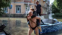 Man with woman on shoulders in flooded Kherson