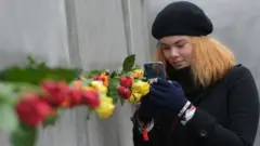 Une fille photographiant un partie du mur de Berlin.
