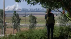 The great aunt of a recently-released hostage stands in a garden while looking out to Gaza in the distance with smoke rising from Israeli shelling, in southern Israel on 6 December.