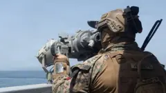 迷彩服を着た米兵が船上から望遠鏡で海上を見ている