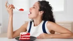 Mulher sentada à mesa, comendo bolo