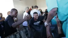 Pessoas choram em volta de corpo carregado para dentro de hospital