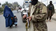 Mulher e criança passam por membros do Talebã em Jalalabad, perto da fronteira com o Paquistão, em foto recente