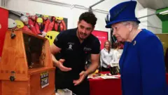 Queen Elizabeth II looking at bees in a hive at a Prince's Trust event while an expert talks to her