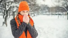 امرأة ترتدي ملابس الشتاء وتحيط أنفها بمنديل