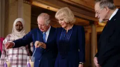 (أشعل الملك تشارلز الثالث والملكة القرينة الشموع في قصر باكنغهام في لندن، جنبًا إلى جنب مع الناجي من الهولوكوست الدكتور مارتن شتيرن والناجية من الإبادة الجماعية في دارفور، أمونة آدم.