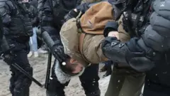 Protester held by police officers