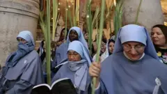 Roman Catholic nuns carry palm branches as they circle the aedicule during the Palm Sunday procession at the Church of the Holy Sepulchre in Jerusalem's Old City, on April 10, 2022. - The ceremony is a landmark in the Roman Catholic calendar, marking the triumphant return of Christ to Jerusalem the week before his death, when a cheering crowd greeted him waving palm leaves. Palm Sunday marks the start of the most solemn week in the Christian calendar. (Photo by AHMAD GHARABLI / AFP) (Photo by AHMAD GHARABLI/AFP via Getty Images)