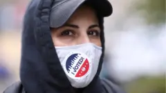 Woman with "I Voted" sticker on her Covid-19 face covering