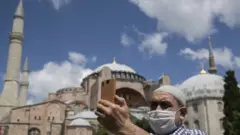 رجل يرتدي كمامة يلتقط صورة لنفسه مع آيا صوفيا في الخلفية
