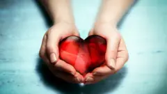A pair of female hands holding red crystal heart