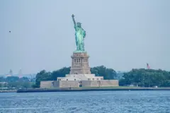 يظهر في الصورة الملتقطة نهاراً تمثال الحرية ذو اللون الأخضر وتعلو اليد شمعة مشتعلة، وسط جزيرة تحيطها مياه ذات موج هادئ وخلفها أشجار يتوسطها العلم الأمريكي.