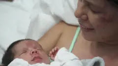 Dayana Patiño mira hacia abajo a su hijo Juan David, quien sonríe desde una cama de hospital en Caracas. Tanto la madre como el bebé presentan heridas en el rostro.