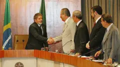 Lula e José Dirceu apertam as mãos, de pé, em um gabinete.