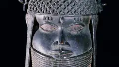 A head of an oba from an ancestral shrine. The head has a high coral collar and a beaded cap with coral clusters in British Museum collection