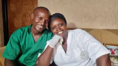 Mukantwari Vestine (iburyo) n'umugabo we. Bicaye mu nzu bamwenyura