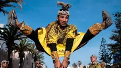 A man jumps in the air as he plays steel hand-held cymbals, called krakebs.
