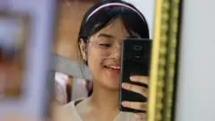 เด็กผู้หญิงใส่แว่นถือโทรศัพท์ส่องกระจก