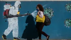 A woman wearing a mask walks past a wall with a graffiti depicting a cleaner in protective gear spraying viruses with the face of President Jair Bolsonaro