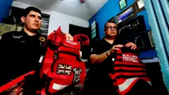 Dois paramédicos, Julio César Vega e Héctor Torres, sentados em uma pequena sala, com seu kit no colo. Ambos vestem uniformes pretos e Torres usa óculos.