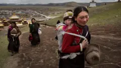 Mulher tibetana carregando bebê nas costas