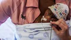 "mère kangourou", tient son fils contre sa peau tandis que
