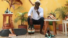Milcos, jeune créateur sénégalais, tenant des chaussures de s marque Nio far