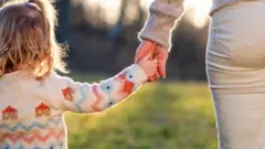 یک دختربچه دست مادرش را گرفته است