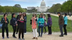 Um grupo de turistas chineses tira fotos com o Capitólio dos EUA ao fundo.