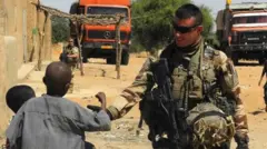 A soldier of France's Barkhane mission stands next to children as he patrols in In-Tillit on November 1, 2017 in Mali