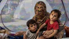 Farzia, 28, who lost her husband in Baghlan one week ago to fighting by the Taliban sits with her children, Subhan, 5, and Ismael ,2, in a tent at a makeshift IDP camp in Kabul