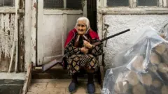 Old woman stands in the entrance of her home with a rifle during the shelling of Stepanakert city