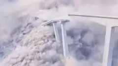 Most zawala się, pozostawiając chmury białego dymu i pyłu; po prawej stronie zdjęcia widać część mostu, która pozostała nienaruszona, a po lewej – fragment, który się zawalił.