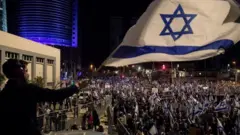 Uwigaragambya azunguza ibendera rya Israel, mu myigaragambyo yitabiriwe n'imbaga y'abantu, yo kwamagana gahunda ya leta yo kuvugurura urwego rw'ubutabera, aha ni Tel Aviv, ku itariki ya 11 y'ukwezi kwa gatatu mu 2023 