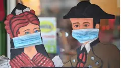 Wooden figures are decorated with surgical masks