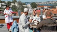 A group of tourists enjoy a meal in Istanbul while a cleaner is standing nearby