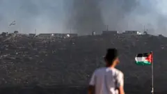 یک نوجوان فلسطینی که در کنار پرچم سرزمینش به یک شهرک یهودی‌نشین در حال ساخت نگاه می‌کند