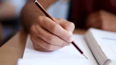 A person grasps a pencil over a book