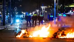 La police se tient près d'objets en feu dans une rue