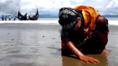 An exhausted Rohingya refugee woman touches the shore after crossing the Bangladesh-Myanmar border by boat through the Bay of Bengal, in Shah Porir Dwip, Bangladesh September 11, 2017.